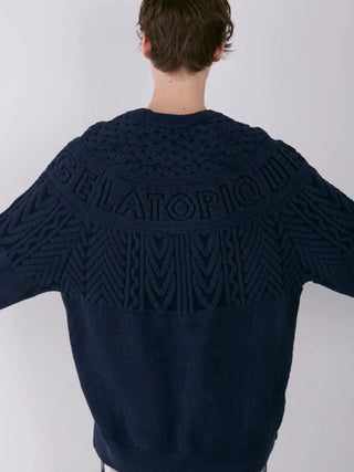 Back view of a model wearing a navy Gelato Pique Aran pullover sweater with intricate knit patterns and lettering.