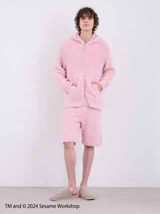 Model wearing pink Sesame Street Elmo hoodie and shorts loungewear set made from fluffy fabric, featuring pockets and a relaxed fit.