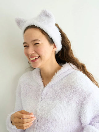 Woman wearing a fluffy white PIQUE MONSTER headband with cat ears, smiling in a cozy plush outfit.