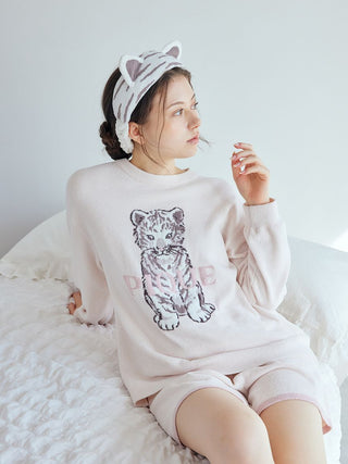 Woman wearing a cozy sweater with a tiger print and a white tiger headband, sitting on a bed, perfect for skincare and relaxation.