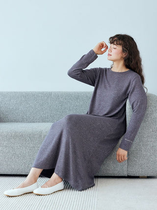 Woman in a Snow Lounge Maxi Dress by Gelato Pique, sitting on a grey couch, exuding elegance and comfort in soft, stretchy fabric.