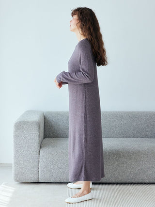 Woman wearing Snow Lounge Maxi Dress, standing by a gray sofa, showcasing relaxed elegance and comfort.