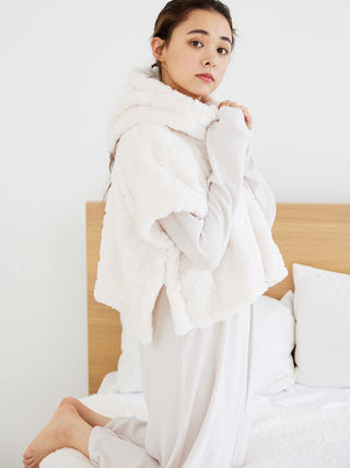 Woman wearing Snow Lounge Maxi Dress with a soft white vest, kneeling on a bed, embodying cozy and comfortable loungewear style.