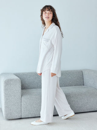 Woman wearing white pajamas stands by a gray sofa in a minimalist room.