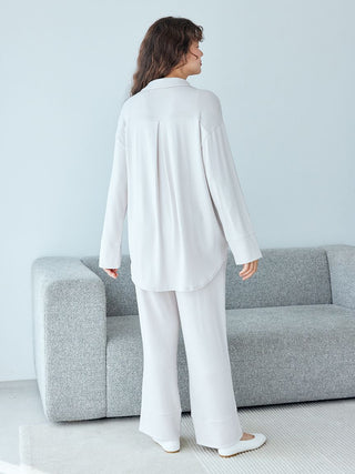 Woman wearing heather gray Snow Lounge Pants and top, standing by a gray sofa, showcasing comfortable and stylish loungewear.