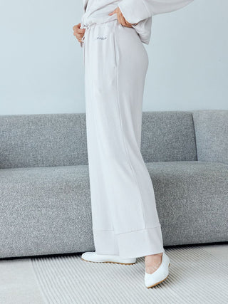 Woman wearing Snow Lounge Pants in heather gray, standing by a gray couch, showcasing the luxurious and breathable fabric.