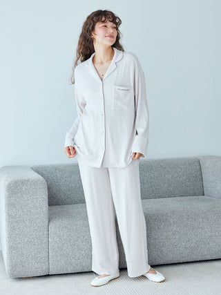 Woman wearing a snow long sleeve pajama shirt, standing next to a gray couch in a relaxed home setting.