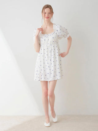 Model wearing a white mini dress with small floral print, featuring a smocked design and puff sleeves for a feminine and elegant look.