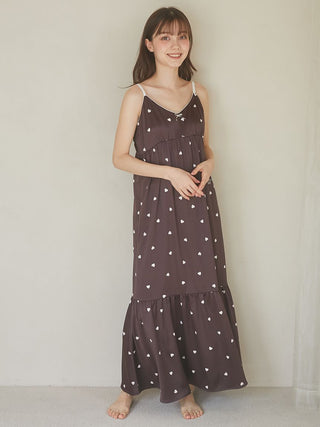 Woman wearing a black satin lounge dress with a heart motif design, standing against a neutral background, showcasing its elegance and comfort.