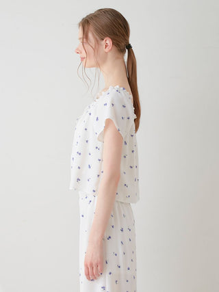 Side view of a woman wearing Gelato Pique's floral print smocked crop top, showcasing the charming blue daisies on a white background.