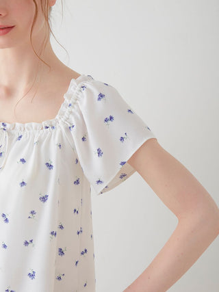 Woman wearing Floral Print Smocked Crop Top with blue daisies on white fabric, featuring a wide elastic neckline.