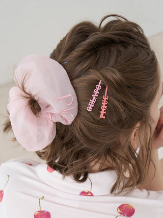 Colorful Gelato Pique hair pins with whimsical logo, adding playful style to brown hair, paired with a soft pink scrunchie.