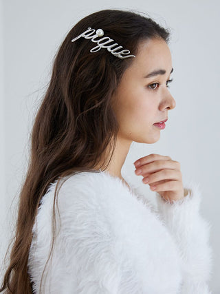 Woman wearing a metal logo barrette with 'Pique' script and pearl accent, shown in side profile with long brown hair.