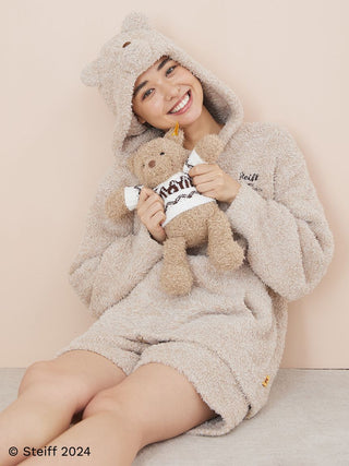 Woman in cozy bear-themed outfit holding Steiff Teddy Bear Jimmy by Gelato Pique, showcasing soft fluffy texture in a warm setting.