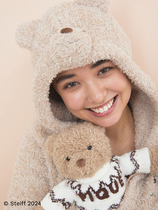 Smiling woman in cozy bear-themed hoodie holding Steiff Teddy Bear Jimmy by Gelato Pique, showcasing soft texture and modern charm.