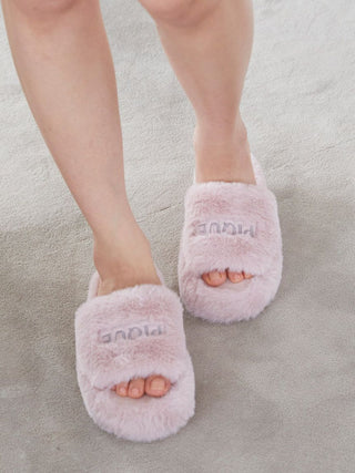 Person wearing pink Eco Fur Fuzzy Slippers with open-toe design, featuring soft faux fur and embroidered logo, on a light carpet.