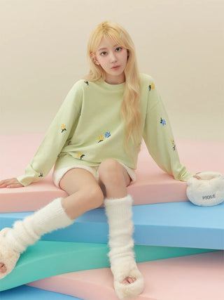 Person wearing fuzzy slippers and a green sweater sitting on colorful steps.