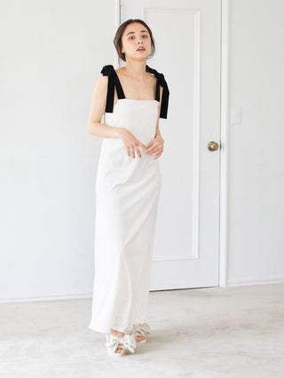 Woman in elegant white dress with black bow straps, wearing luxury velvet bow slip-on shoes, standing in a minimalistic room.