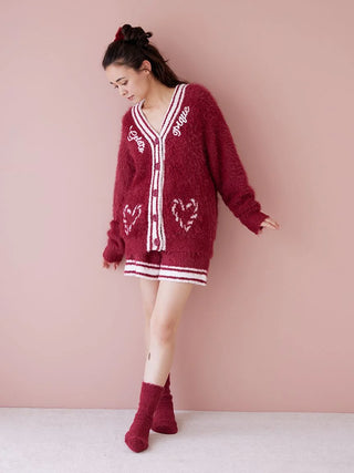 Woman in cozy red sweater and matching fuzzy socks, standing against a pink background, showcasing winter fashion style.