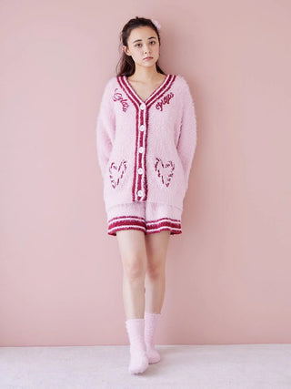 Young woman wearing pink fuzzy cardigan and socks against a pink background, showcasing cozy winter attire.