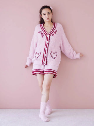 Woman wearing pink fuzzy cardigan and matching socks, standing against a pastel pink background, embodying cozy and stylish comfort.