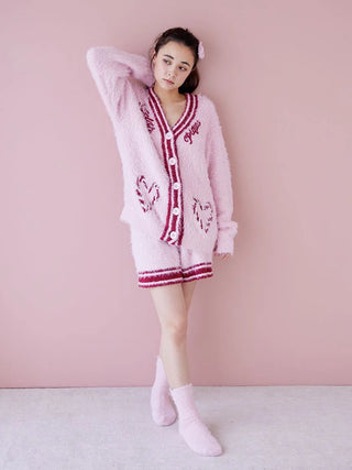 Woman wearing pink fuzzy cardigan and shorts with matching socks, standing against a pink wall.