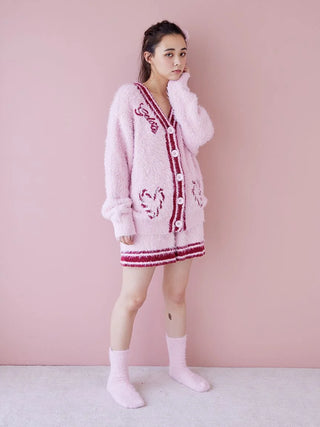 Person wearing cozy pink fuzzy socks and matching cardigan set against a pastel pink wall.