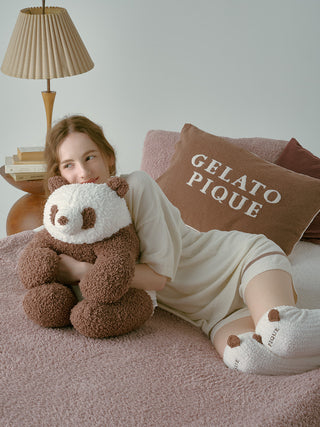 Woman lounging with panda plush and wearing Gelato Pique Panda Long Fuzzy Socks on a cozy bed.