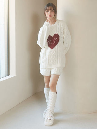 Woman wearing cozy white sweater with heart design, matching shorts, knee-high socks, and Heart Buckle Eco-Fur Bedroom Shoes, standing by a window.