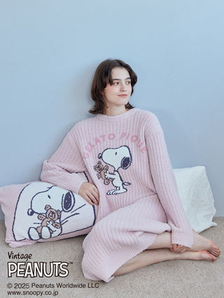 Woman wearing pink Snoopy and Bear Jacquard Lounge Dress from Gelato Pique, sitting with matching Snoopy-themed pillow.