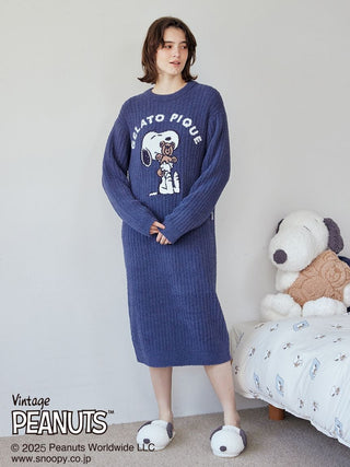 Woman wearing a blue Snoopy and Bear jacquard lounge dress by Gelato Pique, standing near plush Snoopy toys on a bed.