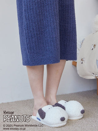 Person wearing a blue jacquard lounge dress with Snoopy slippers on carpeted floor, featuring Peanuts branding.