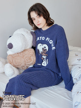 Woman wearing [PEANUTS] SNOOPY×BEAR Jacquard Lounge Dress sitting next to a plush Snoopy toy on a bed.