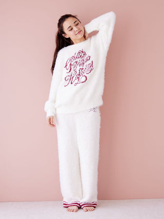 Woman wearing cozy white Feather Lounge Pants and matching top against pink wall, exemplifying winter loungewear style and comfort.