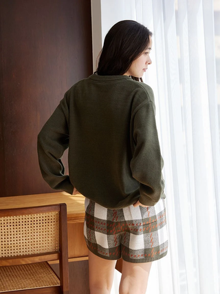 Woman wearing Air Moco Checkered Lounge Shorts by a window, showcasing cozy and stylish multi-colored checkered design.