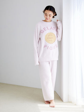 Woman wearing Powder Biscuit Embroidered Lounge Pants and matching top, standing by a sunlit window, enjoying comfort by Gelato Pique.