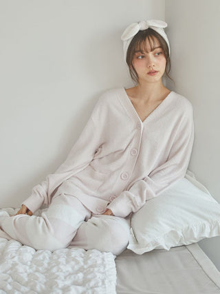 Woman in soft pink oversized cardigan and stylish headband, relaxing on a bed with pillows.