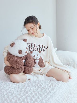 Woman in white Gelato Pique loungewear holding a soft brown and white panda plush, sitting on a bed, embodying cozy premium sleepwear.