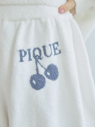 Close-up of white lounge shorts featuring a cherry print and 'PIQUE' text, showcasing soft fabric and playful design.