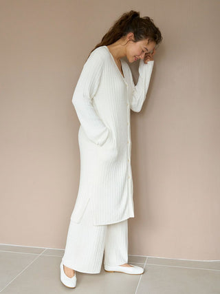 Woman wearing a long ribbed knit button-up cardigan in white, layered over matching knit pants, styled for a cozy and elegant look.