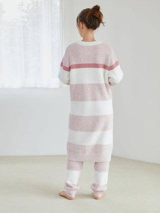 Woman wearing a long, cozy powder melange striped cardigan in soft pink and white, standing in a light-filled room.