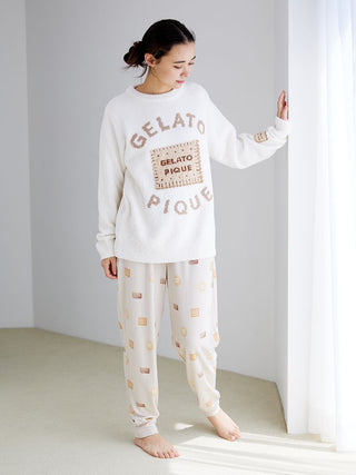 Woman wearing Gelato Pique Powder Biscuit Jacquard Pullover Sweater, cozy white with biscuit design, standing by window.