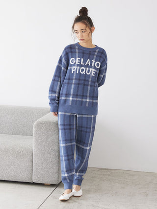 Woman wearing Gelato Pique checkered pajama set in pastel tones, standing by a sofa, showcasing cozy loungewear fashion.