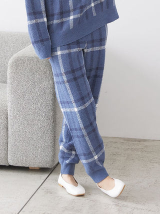 Woman wearing a blue checkered pajama set standing by a grey couch, showcasing comfortable and stylish loungewear.