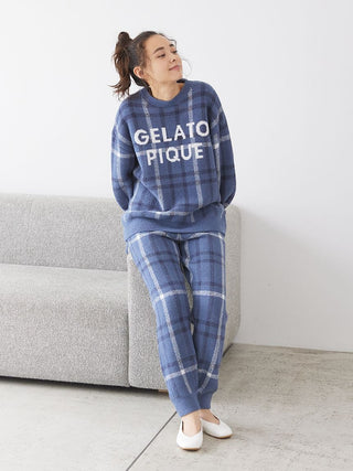 Woman wearing Gelato Pique Checkered Pajama Set in blue, leaning against a sofa, showcasing relaxed fit and comfort style. Cozy loungewear.