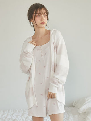 Woman in pink outfit wearing a light striped cardigan, standing in a cozy bedroom setting.