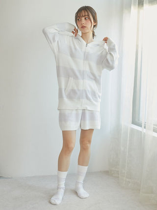 Model wearing a white striped zip parka and shorts, showcasing a casual and comfortable style indoors.