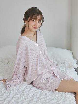 Woman wearing pink ribbed shorts and cardigan set sitting on bed