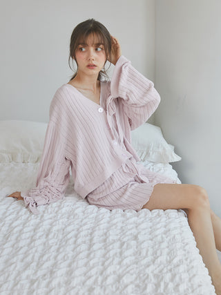 Woman wearing 2025 ribbed shorts in soft pink, sitting on a bed, styled with a matching ribbed cardigan for a feminine look.