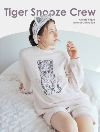 Woman in cozy tiger print loungewear from Gelato Pique Animal Collection, sitting on a bed with a tiger headband, 'Tiger Snooze Crew' text.